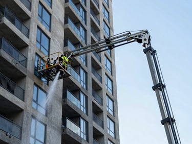 Technician operating a water-fed pole system on a multi-storey South Shore apartment building exterior, clear sky background, stream of purified water visible on the glass
