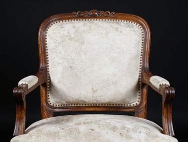 Close-up straight-on studio shot of a carved 17th-century French walnut armchair, even white light revealing joinery details and worn upholstery patina, black background, no props
