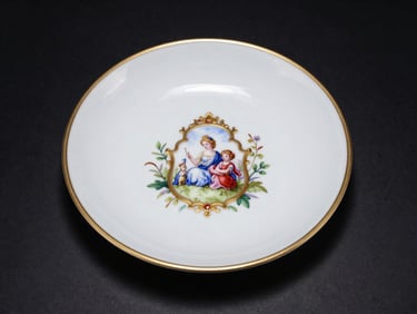 Overhead studio shot of a Meissen porcelain centerpiece, controlled spotlight isolating gilded rim detail and hand-painted cartouche against a pure black surface, no background clutter