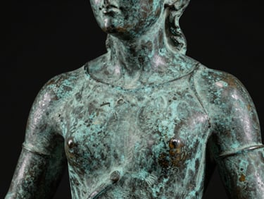 Macro studio photograph of a 19th-century bronze sculpture detail, raking light across the patinated surface revealing casting texture and foundry marks, jet black background, no staging