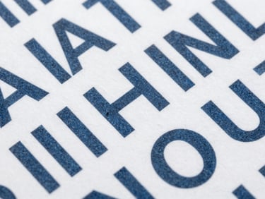 Close-up macro shot of structured typographic layout on thick white cardstock, slate ink, clean geometric grid lines, flat lighting