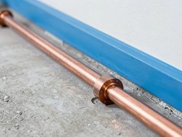 Crisp commercial photography of newly installed copper and PVC pipelines under a concrete slab, perfectly aligned and clean, bright indoor light.