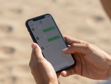 Close-up of hands holding a smartphone displaying a chat, warm natural outdoor daylight, soft sand-colored background, shallow depth of field.