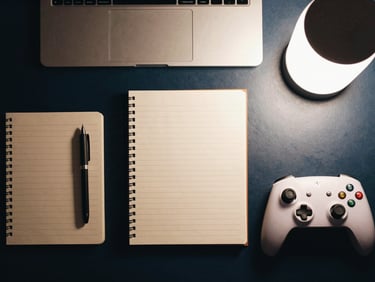 An overhead flat-lay of neatly organized physical workspace tools, notebooks, and a controller, moody lighting