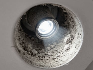 Close-up macro shot of residential AC duct interior, thick grey dust coating every surface under bright flashlight, fibres and debris visible in sharp detail, overhead angle inside the duct