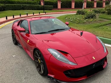 A red Ferrari 812 Superfast luxury sports car parked on a paved driveway in front of a Mediterranean-style resort.