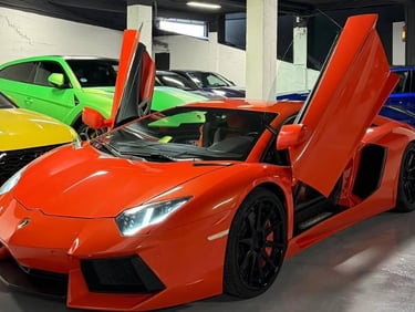 Orange Lamborghini Aventador with scissor doors open in a luxury car showroom garage.