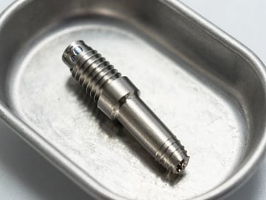 Close-up photograph of a Nobel Biocare dental implant fixture in titanium resting on a sterile surgical tray under operating-room lighting, clinical white background, no hands