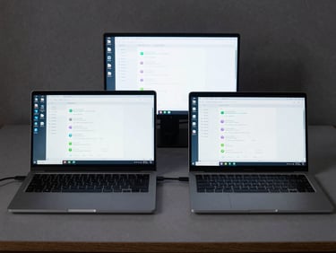 Wide overhead shot of a developer workstation showing two Android devices side by side on a grey desk, screens displaying compatibility test results and device logs, even diffuse studio lighting, no people, technical workspace context