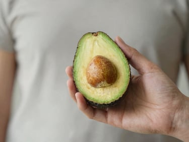 Close-up of a human hand holding a ripe avocado, soft natural light, shallow depth of field, muted organic tones.
