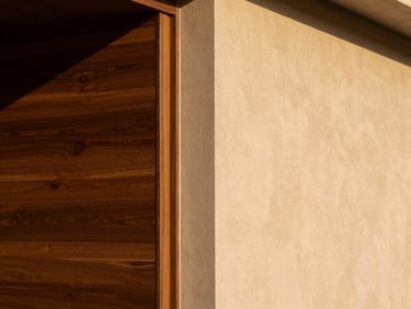 Straight-on architectural detail shot of a wall transition inside a Riyadh villa. Rich bronze-toned wood alternative panels meet a flawlessly finished warm plaster wall. Soft morning side-light highlighting the rich textures and clean joints.