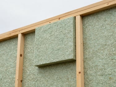 Close-up of high-performance wood-fiber insulation boards being installed on a timber frame, soft overcast UK daylight, 35mm lens