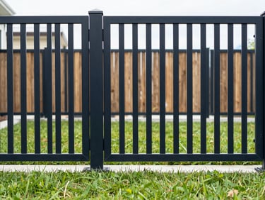 A modern black ornamental aluminum fence with clean geometric lines, framing a manicured lawn under crisp daylight, architectural photography, 35mm