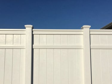 A clean white vinyl privacy fence set perfectly straight against a deep blue afternoon sky, sharp architectural focus, bright natural daylight, 35mm