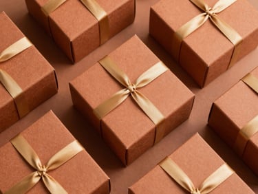 Styled flatlay of luxury cartonage boxes in warm terracotta and clay tones, displaying perfect geometric alignment and elegant gold ribbon details, soft side lighting.
