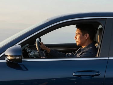 Side profile of a professional driver in a clean suit steering a premium vehicle, soft morning light, clean and calm atmosphere.