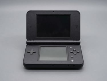 Straight-on product shot of a matte black refurbished DSi console resting on a graphite surface, clean industrial lighting.