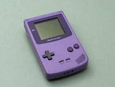 A clear purple Game Boy Color console showing its internal circuit board, resting on a muted green background.