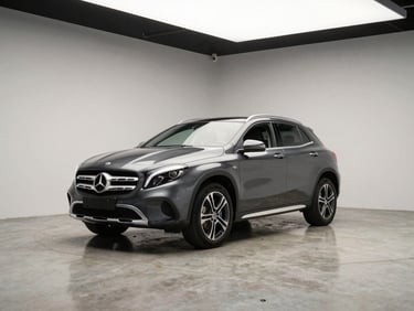 Three-quarter front angle of a dark grey Mercedes-Benz GLA on a wide matte concrete studio floor, clean overhead strobes, minimal neutral background, no people
