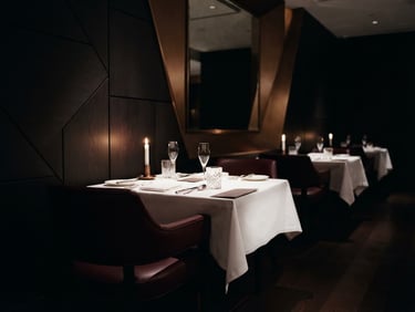 luxury editorial photography of a pristine empty fine dining room with sharp architectural angles, dramatic low-key side lighting, deep shadows, 35mm