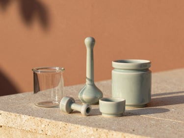 Elegant ceramic smoking accessories and minimalist glass jars resting on a textured stone surface, soft terracotta background, warm light