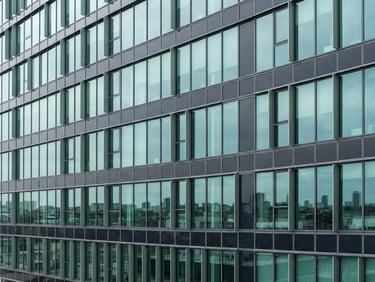 Clean architectural detail of a modern energy-efficient corporate building facade with integrated solar panels, sharp glass lines, bright overcast daylight, cool teal and sage reflections.