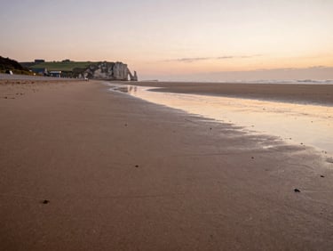 Wide sandy beach of Normandy at dusk, soft tide pools reflecting a pastel sky, distant cliffs, peaceful atmosphere