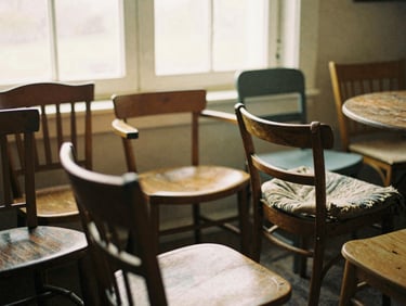 Close-up of a collection of mismatched vintage wooden chairs around a table, soft golden light.