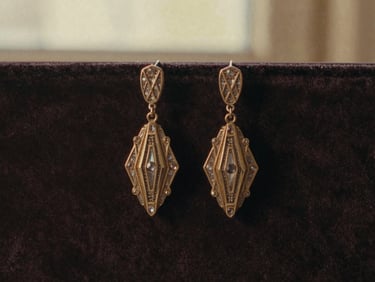 Close-up of a pair of Art Deco drop earrings with geometric patterns and small gemstones, on a dark velvet background.