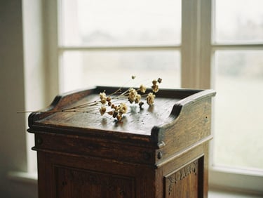 Close-up of an antique oak lectern, intricate carvings, aged wood texture, soft window light, dried flowers on top.