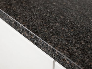 Macro overhead shot of an immaculate, polished dark granite countertop with a sharp geometric corner, bright studio lighting.