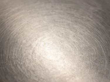 A close-up macro shot of an immaculate, streak-free stainless steel surface under bright, clean studio lighting with zero warm filters.