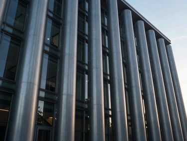 Wide-angle structural glass and steel columns of a civic building, cool morning light.