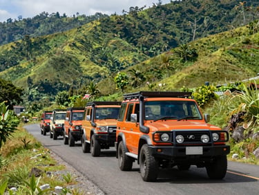 A professional convoy of modern 4x4 vehicles driving on a clean paved mountain road in Sumatra, lush green hills, bright daylight, 35mm lens.
