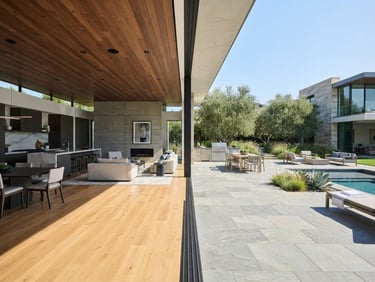 Wide-angle architectural photograph of a modern home interior transitioning to an exterior stone patio, crisp natural daylight, sharp material joins, editorial style.