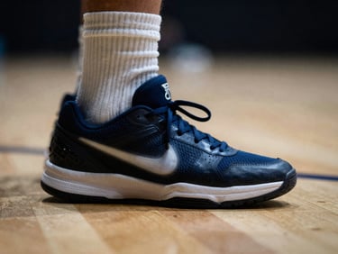 Close-up of technical footwork on an indoor court, motion blur on the sneakers, harsh overhead spotlight, deep shadows.