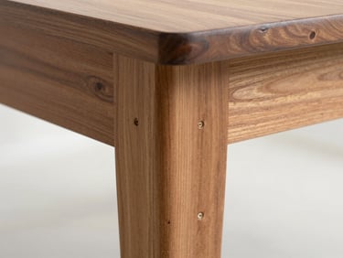 Close-up detail shot of hand-cut teak mortise and tenon joint on a custom dining table leg, even midday light, white workshop background, no tools in frame