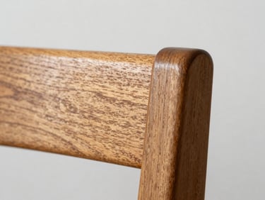 Close-up macro of teak dining chair corner joint under even north-facing daylight, wood grain and dovetail joinery clearly visible, white wall background, no styling