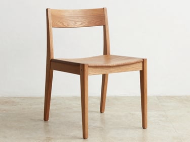 Close environmental shot of a solid teak dining chair against a white wall under even daylight, wood grain and mortise-and-tenon joinery clearly visible, no fabric or cushion, pale stone floor