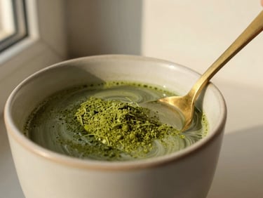 A clean ceramic cup of warm water with a vibrant green Moringa powder swirl, soft side window light, matte gold spoon resting beside it, 35mm