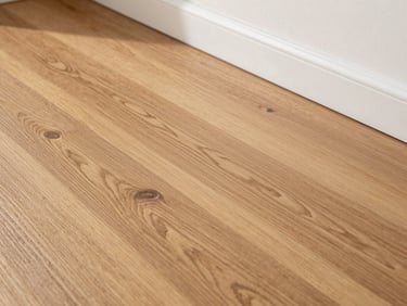 A finished oak hardwood floor reflecting soft daylight, meeting a clean white baseboard.