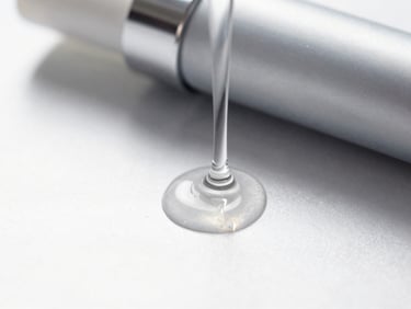 Close-up high-key studio shot of liquid cosmetic gel dripping over a reflective silver surface, clean technical lighting, sharp focus, 35mm