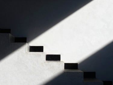 An abstract close-up of a minimalist concrete staircase casting sharp diagonal shadows, clean architectural lines, high-contrast natural light, deep navy shadows and bright white surfaces.