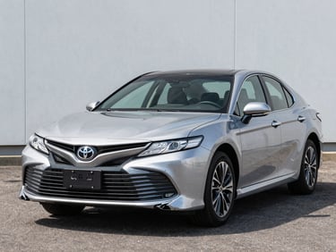 2019 Toyota Camry silver sedan photographed three-quarter front on clean tarmac, bright daylight, no people, full vehicle visible