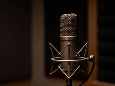 Close-up of a vintage condenser microphone in an acoustically treated recording booth, moody low-key lighting, deep shadows, warm amber accent light.