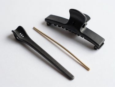 Tight overhead arrangement of hair accessories on white surface — a sculptural clip, a minimal hair pin, a thin elastic — bright studio light showing material finish and construction at close range
