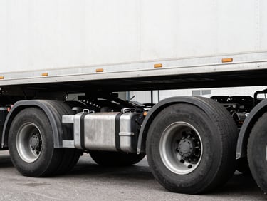 Close-up of a semi-trailer truck's undercarriage, focusing on suspension and axle components, high-contrast garage lighting, desaturated tones, sharp focus.