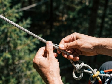 Hands tying a complex climbing knot with a dynamic rope, close-up technical details
