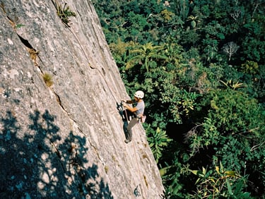 Wide-angle action shot of a climber rigging ropes on a steep rock face in Zapopan, harsh natural sunlight casting sharp shadows, deep forest greens, 35mm film.