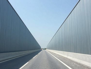 Wide environmental shot of a highway construction corridor under bright daylight, clean architectural lines, cool blue tones, 35mm